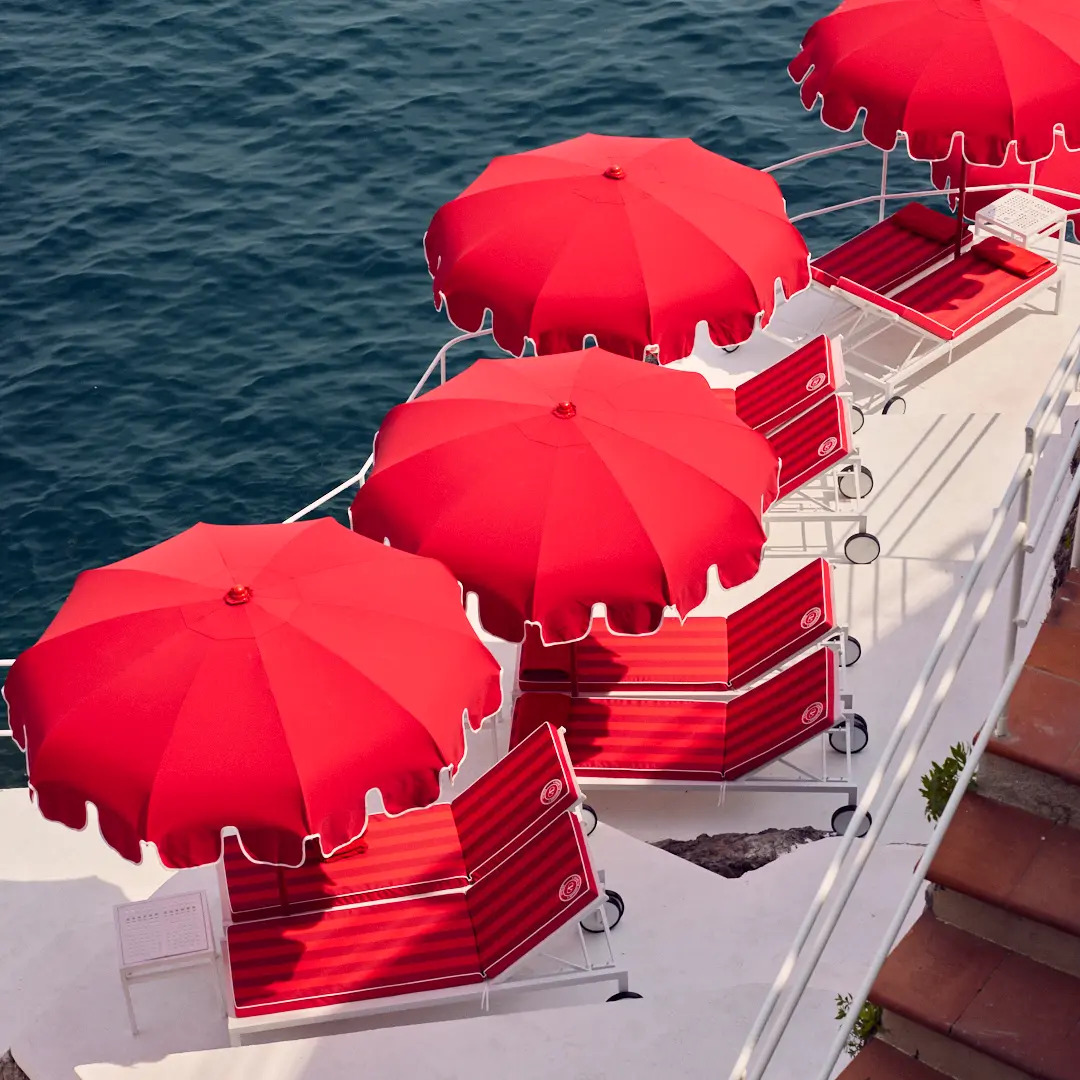 Aerial view of red lounge chairs and red umbrellas overlooking the sea at a cliffside beach club